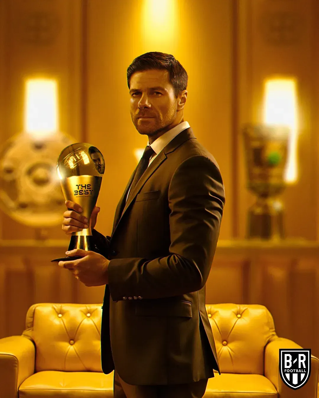 Xabi Alonso en costume tenant le trophée du meilleur entraîneur dans un salon doré